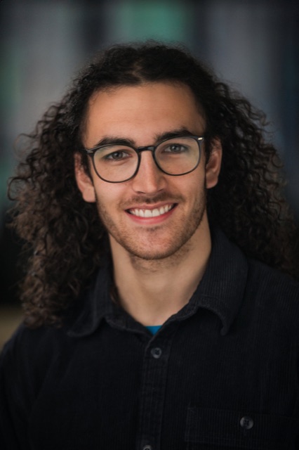 Dewi Erwan smiling, with long curly hair and glasses